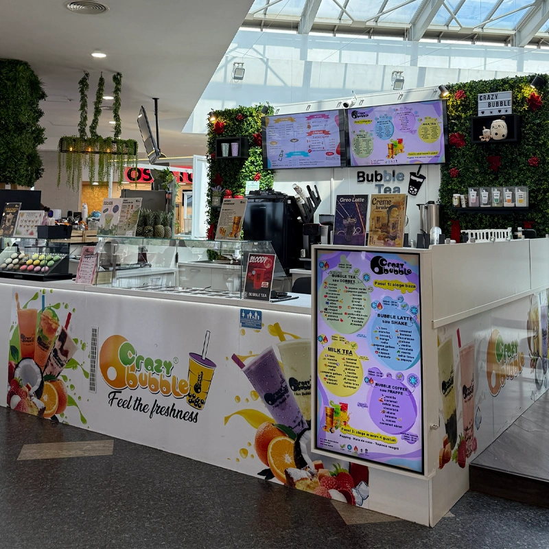 Bubble tea kiosk in a bright mall, large colorful menu boards, and a counter displaying drinks and fruit graphics with 'Crazy Bubble' branding.