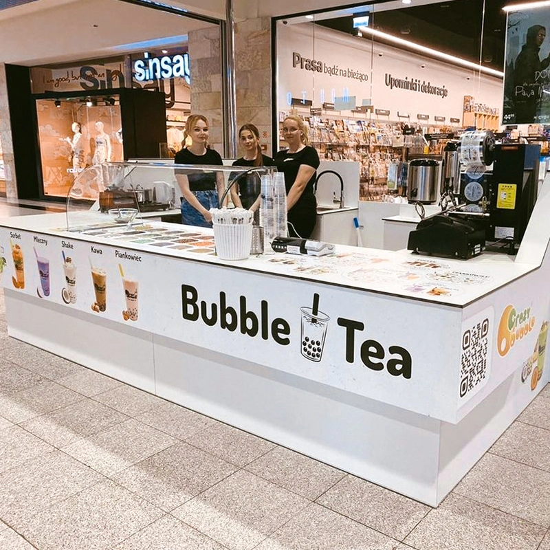 Bubble Tea kiosk in a mall with three staff behind the counter; drink images on the front panel.