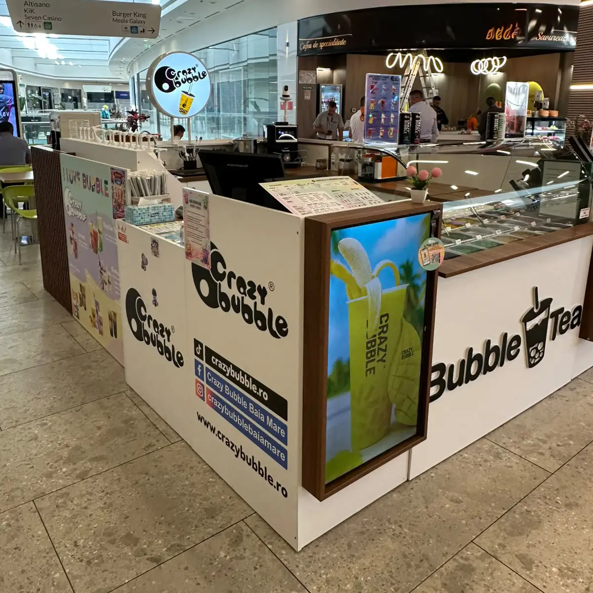 A Crazy Bubble beverage kiosk in a mall with white counters, large Crazy Bubble logos, a beverage poster on the front, and a glass display case.