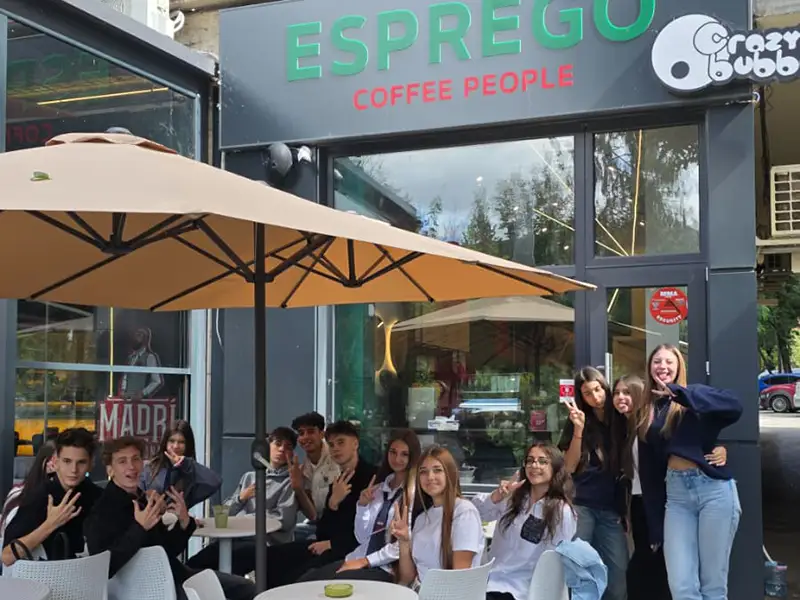 Group of teens posing outside Esprego Coffee People cafe under a large beige patio umbrella.