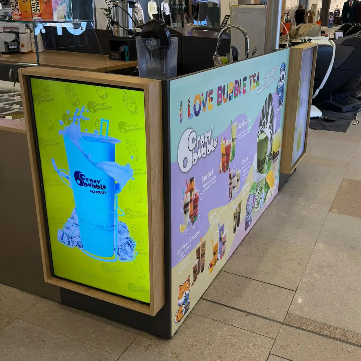 Colorful bubble tea kiosk in a mall, with bright lime panel showing a blue drink and a pastel menu panel reading 'I Love Bubble Tea' and featuring various drinks.
