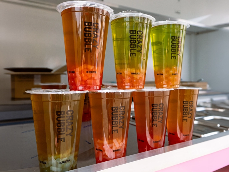 Six clear plastic cups with orange-to-pink and green-to-orange gradients labeled 'Crazy Bubble' on a shelf.