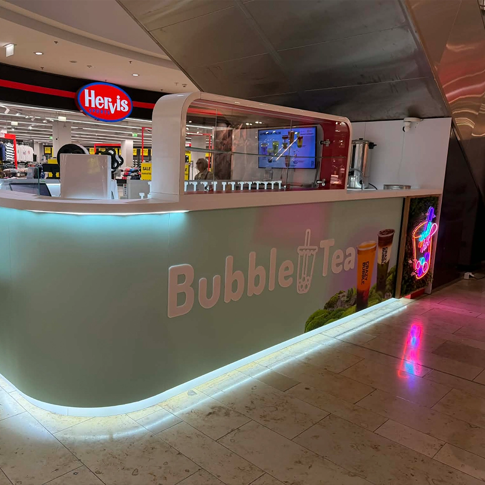 Bubble Tea kiosk in a mall, pastel green curved counter with underlit edge and neon sign on the right.