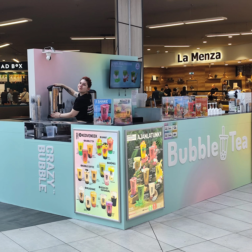 Colorful Bubble Tea kiosk in a mall with a smiling barista preparing a drink; large 'Bubble Tea' sign on the counter.