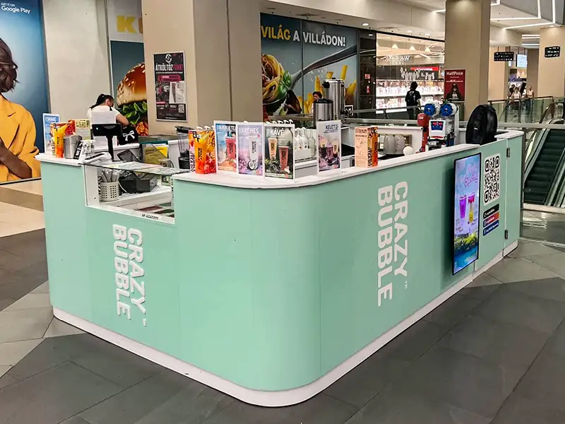 Mint-green Crazy Bubble kiosk in a shopping mall, with drink menu posters on top and a QR code on the side.