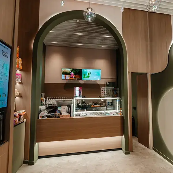 A cafe counter framed by a dark green arched doorway, with a glass display case and beverage bar behind it.